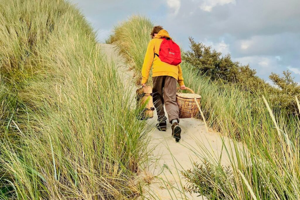 Olivier sjouwt picknickmanden over het duinpad voor de schemerwandeling van Eilandmeisje